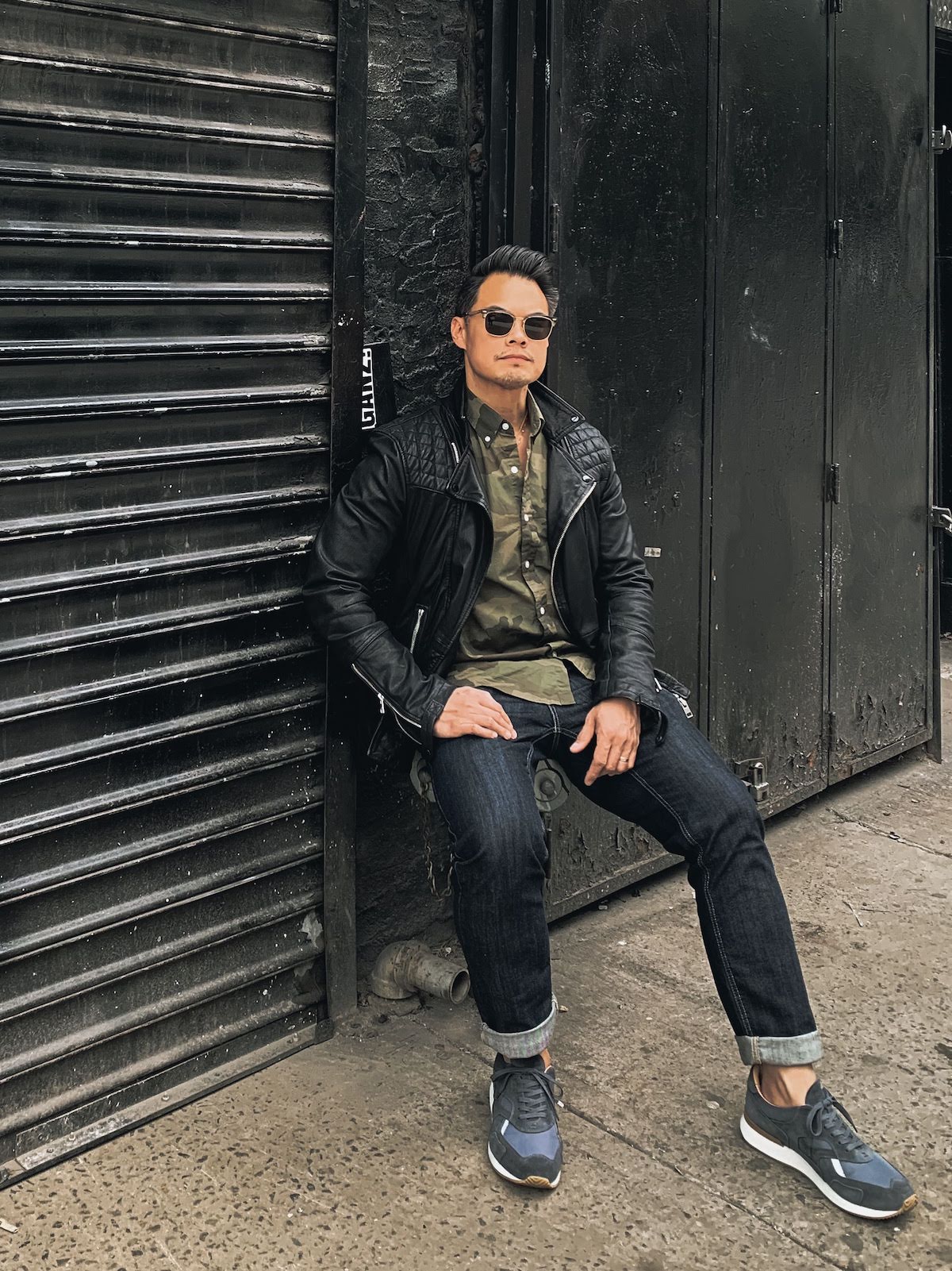 man wearing black leather jacket and camo shirt with dark blue jeans