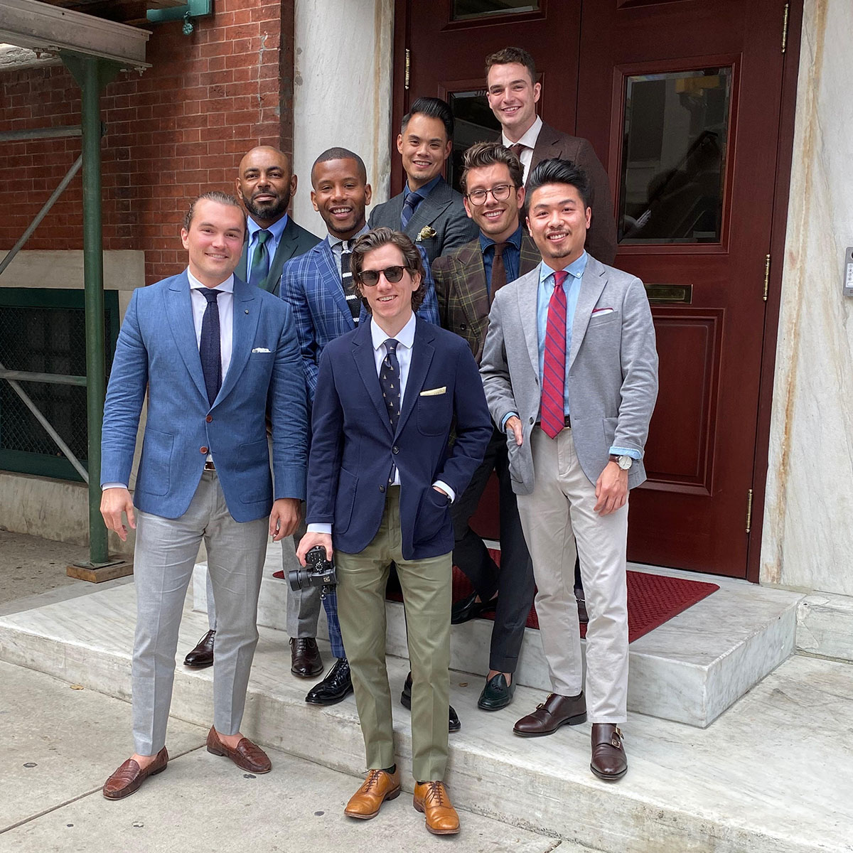 group of men wearing suit jackets and ties standing in front of brown door
