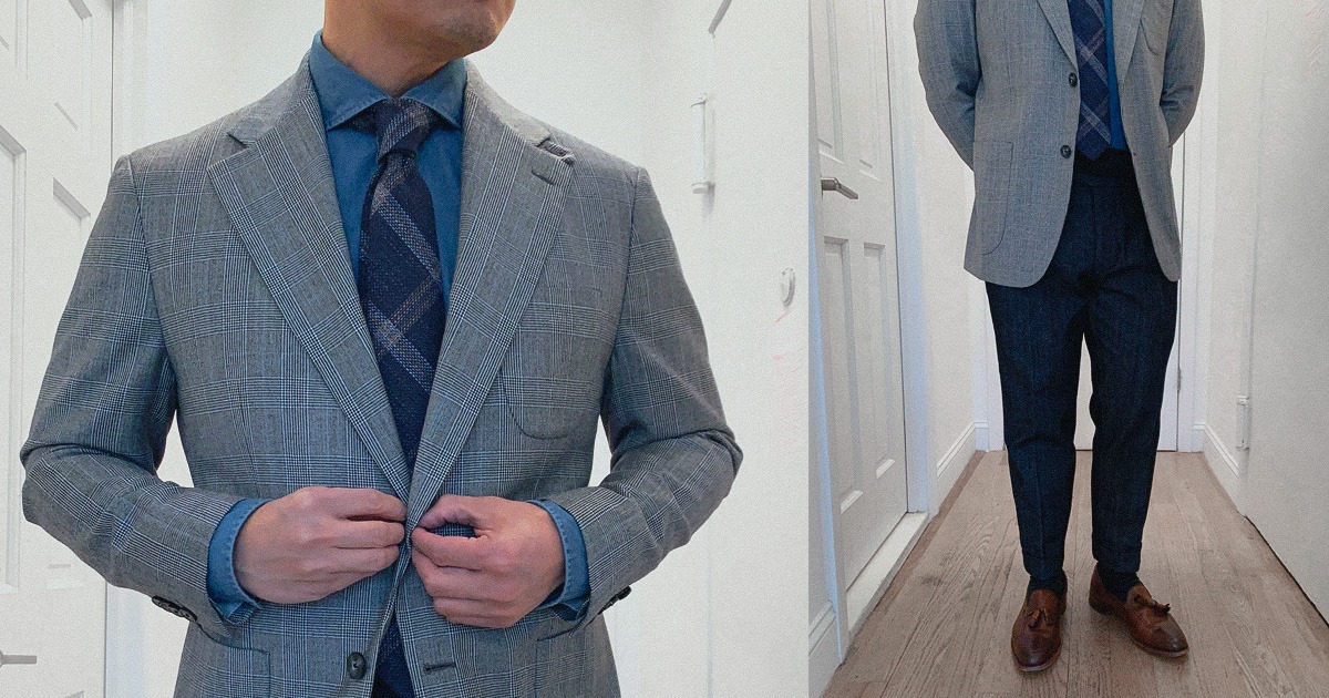 closeup of man's grey plaid suit jacket blue shirt blue plaid tie and dark trousers and brown shoes