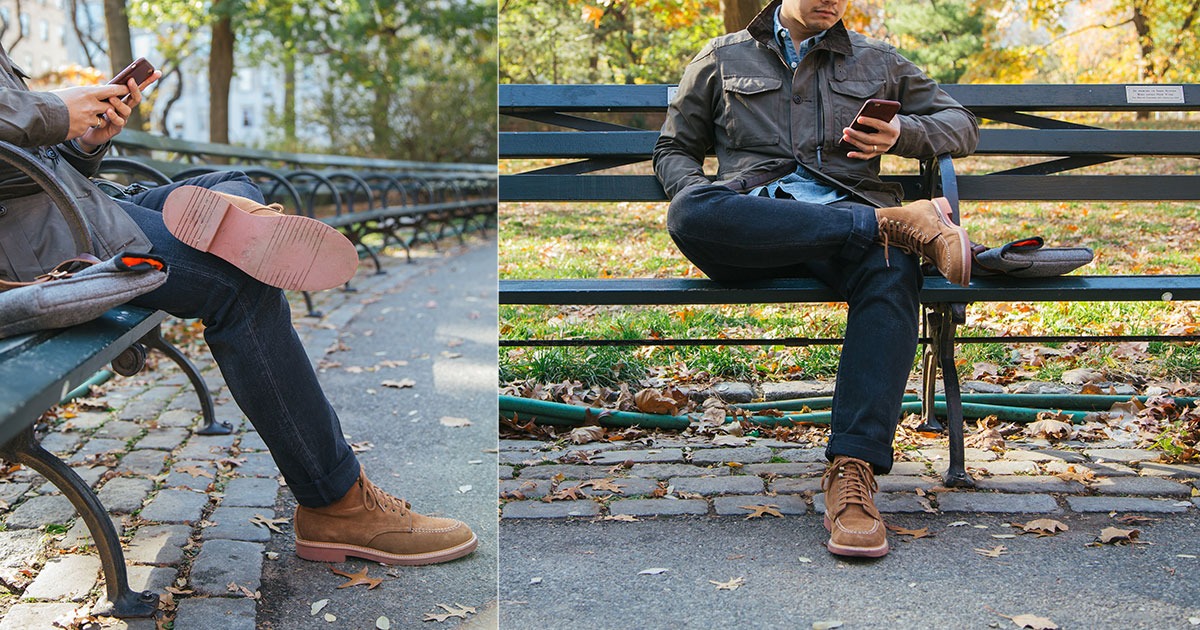 man on park bench wearing jeans and brown boots sitting with legs crossed