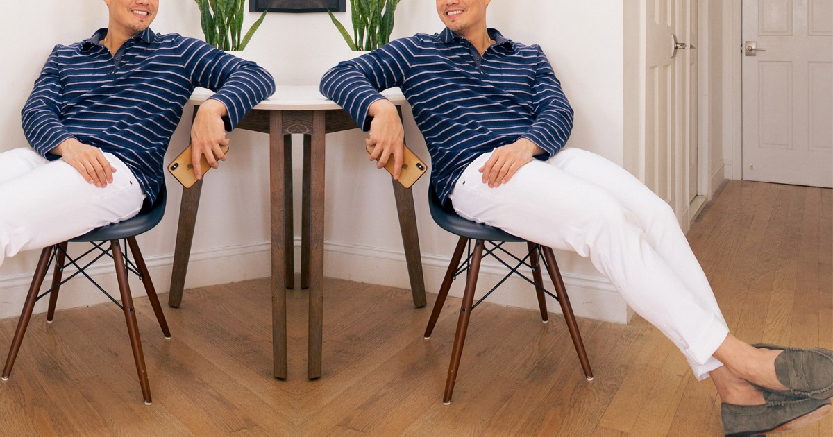 man in blue long sleeve shirt and white jeans and green loafers leaning back in chair