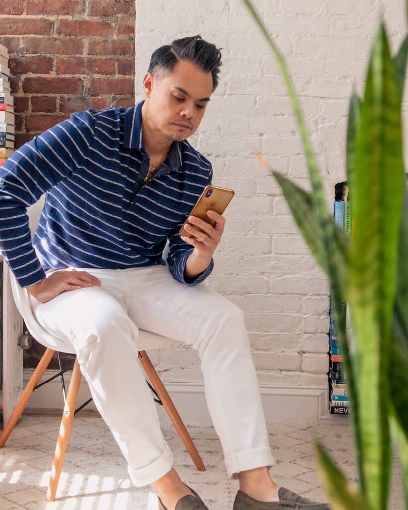 asian man in dark blue polo and white jeans on phone