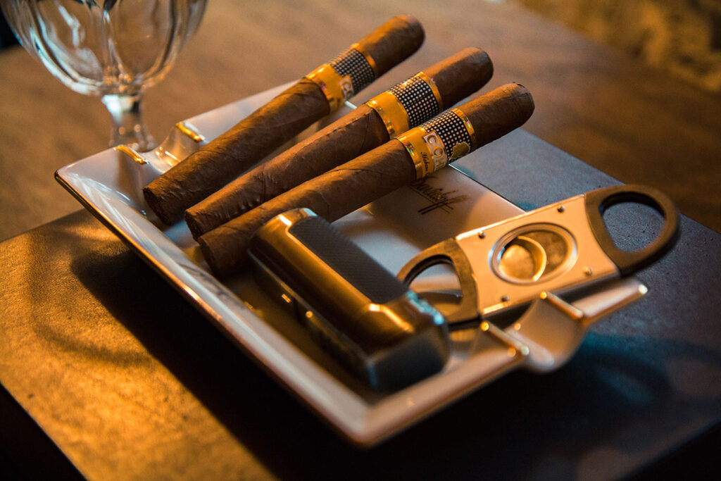 3 cigars a cutter and a lighter in an ashtray